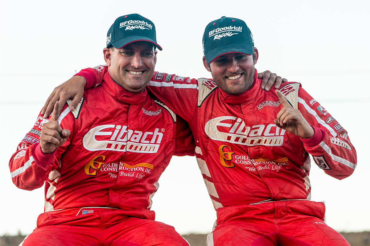 Team Eibach racers Jason Coleman and Brady Melin posing with their arms around each other, both holding up a finger to indicate first place.